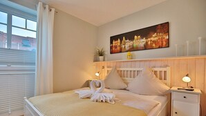 A hotel room with a bed, a nightstand, a wall-mounted lamp, a painting, and a window with blinds.