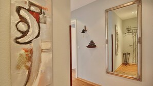 A hallway with a large abstract painting, a mirror, and a small decorative shelf.