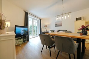 A modern living room with a flat-screen TV, dining table, and chairs.
