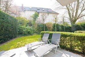 A patio with two lounge chairs and a table, surrounded by well-maintained hedges and a lawn. - Villa am Meer Strandallee 48 Apartment 3 - Villa am Meer (Timmendorfer Strand)