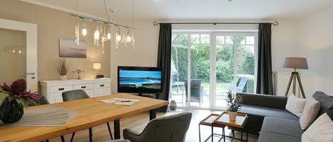 Una sala moderna con una mesa de comedor de madera, un sofá gris y un televisor.