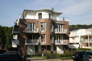 A multi-story residential building with balconies, brick facade, and a parking area in front.