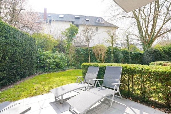 A patio with two lounge chairs and a table, surrounded by well-maintained hedges and a lawn.