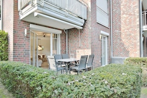 A brick building with a patio area featuring a table and chairs, a glass door entrance, and a small garden area.