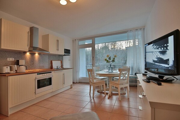 A modern kitchen with white cabinetry, a dining area with a round table and chairs, and a television on a stand.
