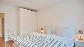 Un dormitorio con cama, armario blanco, lámparas de noche y una silla.