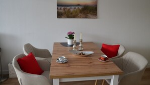 Un comedor con una mesa de madera, dos sillas, un cuadro de una playa y un florero con flores.