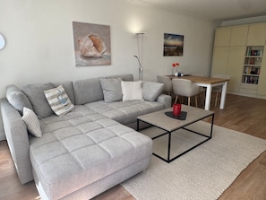 Una sala de estar moderna con un sofá seccional gris, una mesa de centro y un comedor con una mesa de madera y sillas.