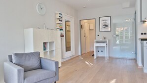 Una sala de estar moderna con un sofá gris, una estantería blanca y una zona de cocina con una mesa de comedor.