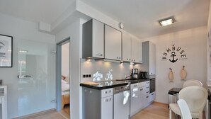 Una cocina moderna con armarios grises, una encimera negra y una cafetera. Hay una zona de comedor con una silla blanca y una mesa.