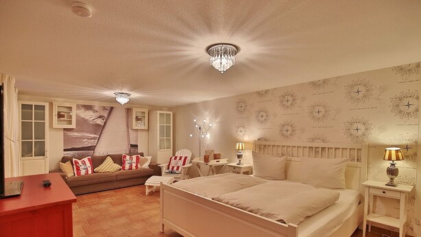 Ein Schlafzimmer mit einem großen Bett, einem Nachttisch, einem Sessel, einem Schreibtisch und einer roten Kommode.
