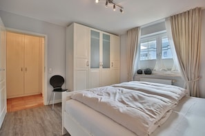 Quarto com cama, guarda-roupa, cadeira e janela com cortinas.