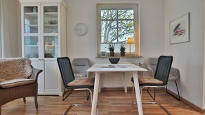 Ein Essbereich mit weißem Tisch, zwei Stühlen, einem Schrank und einem Fenster mit Pflanzen.