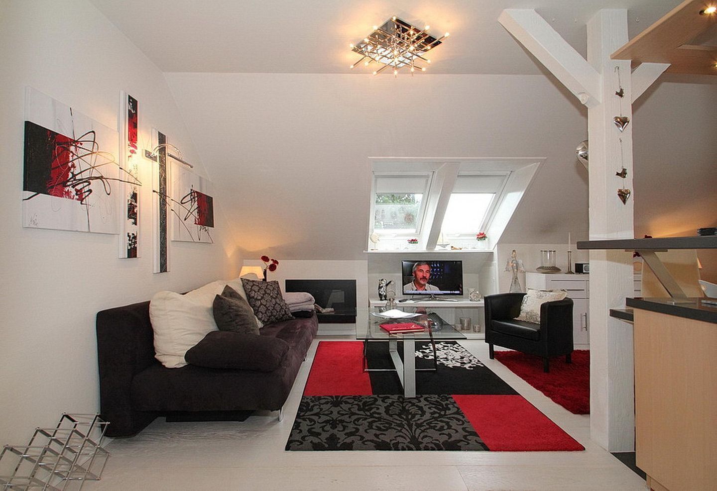 A modern living room with a dark sofa, a coffee table, and a TV. There are abstract paintings on the wall and a red rug on the floor.