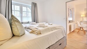 A modern bedroom with a large bed, a bedside table, a chair, and a view of the outdoors through a window.