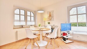 A modern dining area with a round table, white chairs, and a TV on a stand.