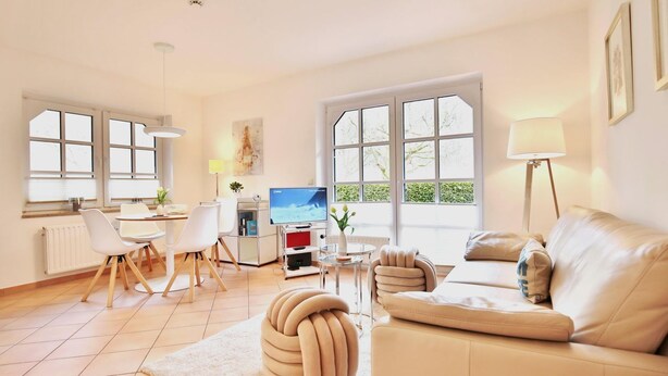 A modern living room with a sofa, a dining table with chairs, a TV, and large windows.