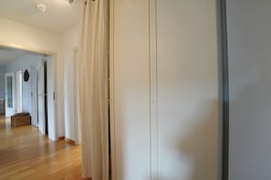 A hallway with a wooden floor, white walls, and a door with a curtain.