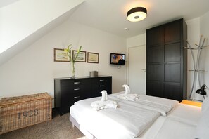 A bedroom with a bed, a dresser, a television, a coat rack, and a wicker basket.