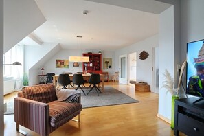A modern living room with a sofa, dining table, chairs, and a television.