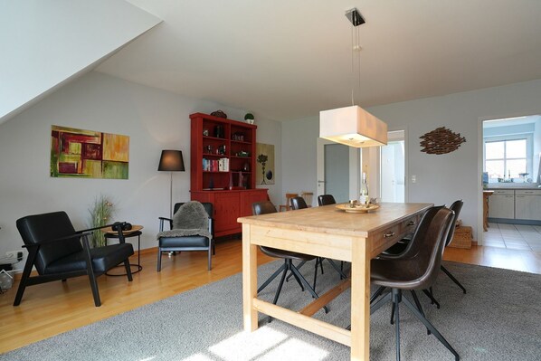 A modern living room with a dining table, chairs, a red bookshelf, and a large painting on the wall.