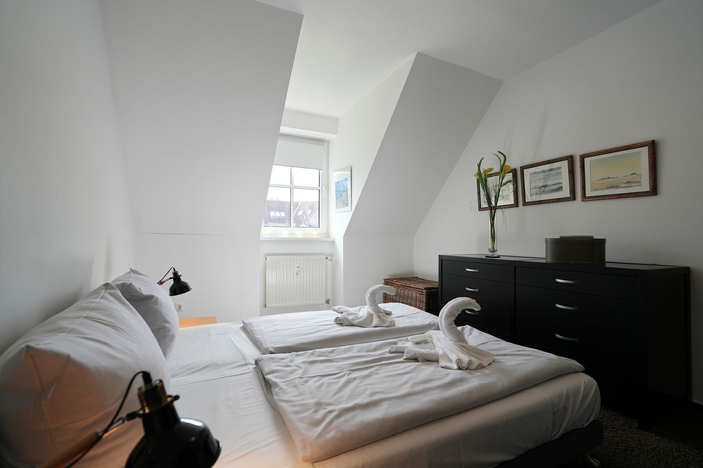 Ein Hotelzimmer mit zwei Betten, einem Schminktisch, einer Heizung und gerahmten Bildern an der Wand.