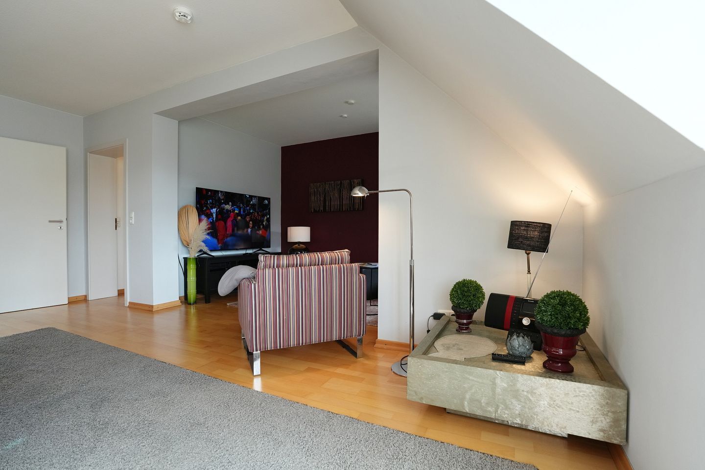 A modern living room with a sofa, a flat-screen TV, a lamp, and a small table with decorative items.