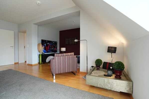 A modern living room with a sofa, a flat-screen TV, a lamp, and a small table with decorative items.