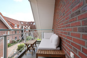 A balcony with a wooden table and white sofa, overlooking a brick building with red-tiled roofs.