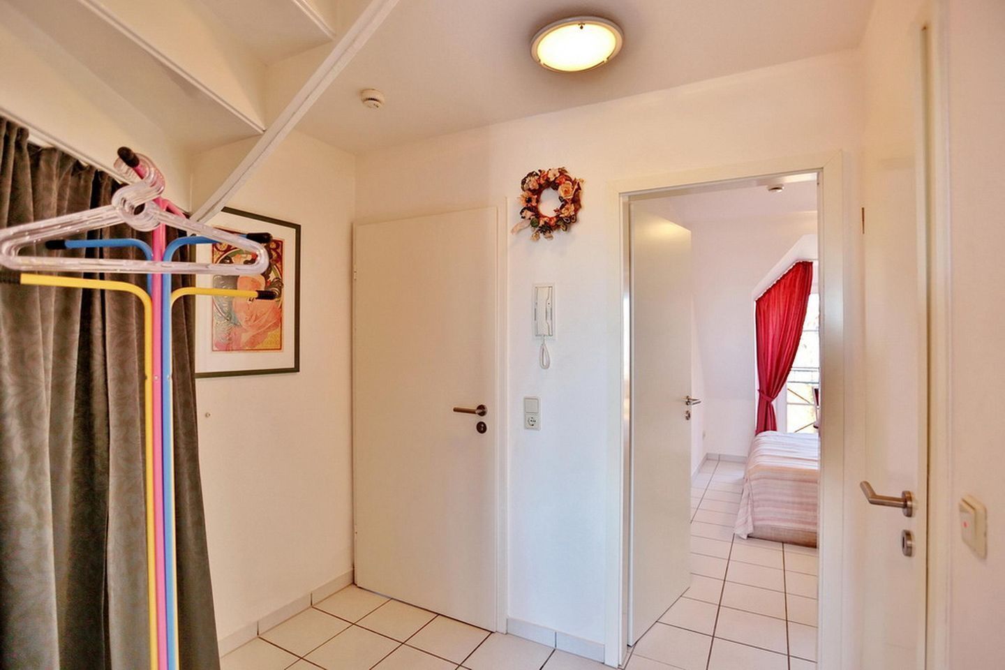 Habitación de hotel con una puerta blanca, un cuadro enmarcado, un teléfono y una cortina roja.