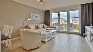 A modern living room with a sofa, a coffee table, and a lamp. There is a large window with curtains and a view of the outside.