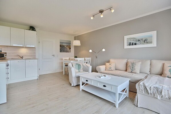 Un salon moderne avec un canapé blanc, une table basse et un coin repas avec des chaises blanches.