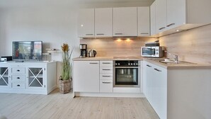 A modern kitchen with white cabinetry, a built-in oven, a microwave, and a coffee maker.