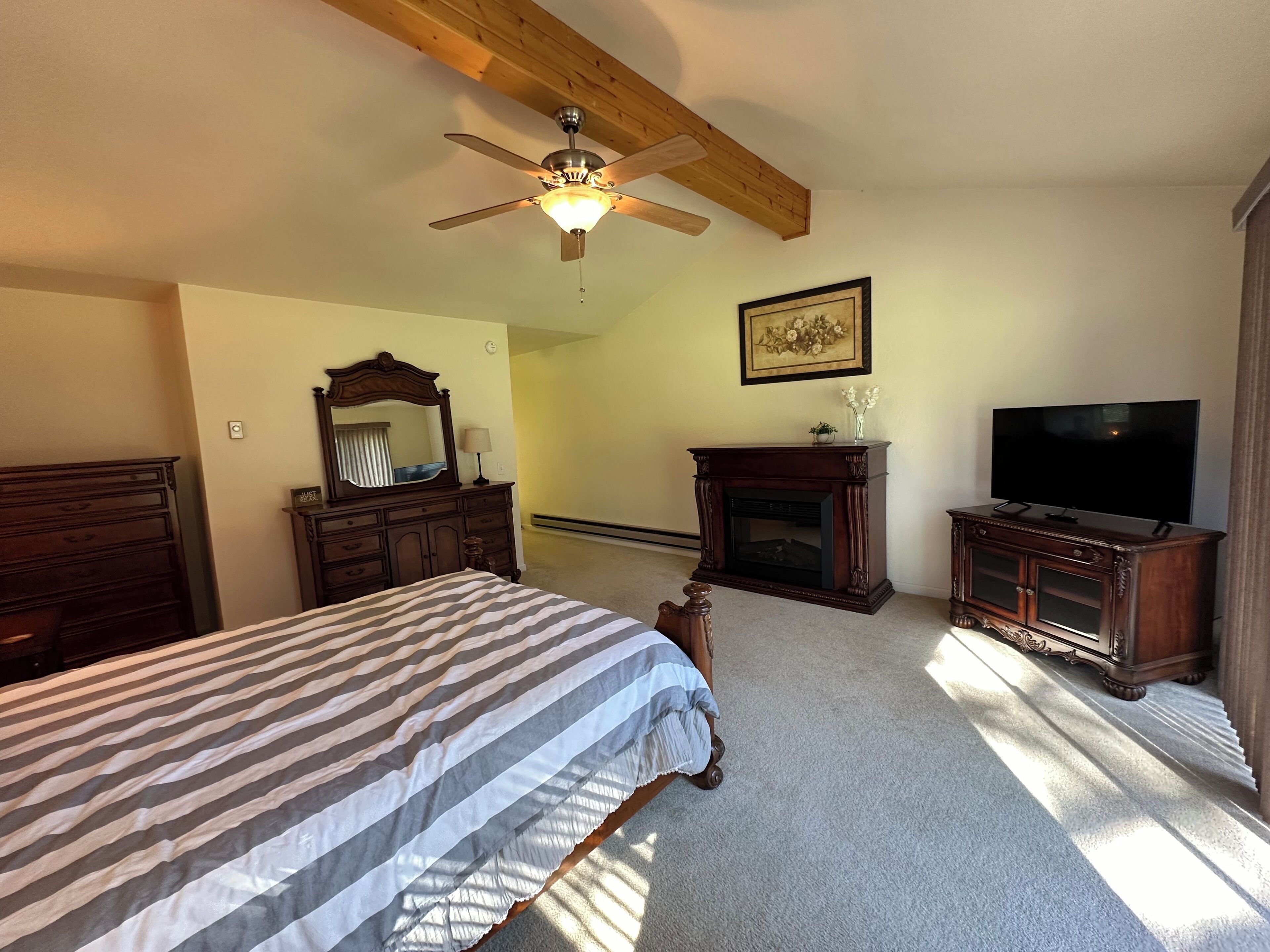 A bedroom with a bed, a ceiling fan, a fireplace, a television, and a mirror.