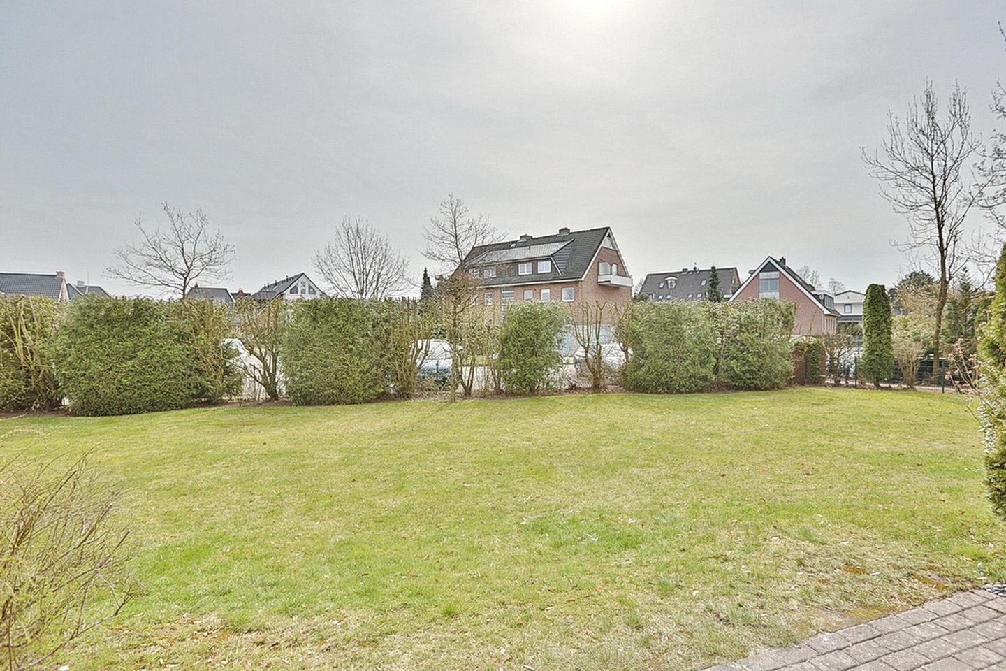A residential area with a large grassy lawn, a house with a sloped roof, and a hedge in the foreground.