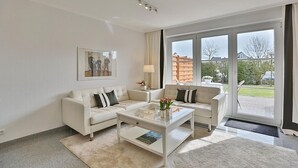 Un salon moderne avec deux canapés blancs, une table basse en verre et un tableau encadré accroché au mur.