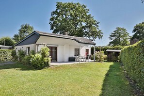 A single-story house with a covered patio, a lawn, and a large tree in the background.