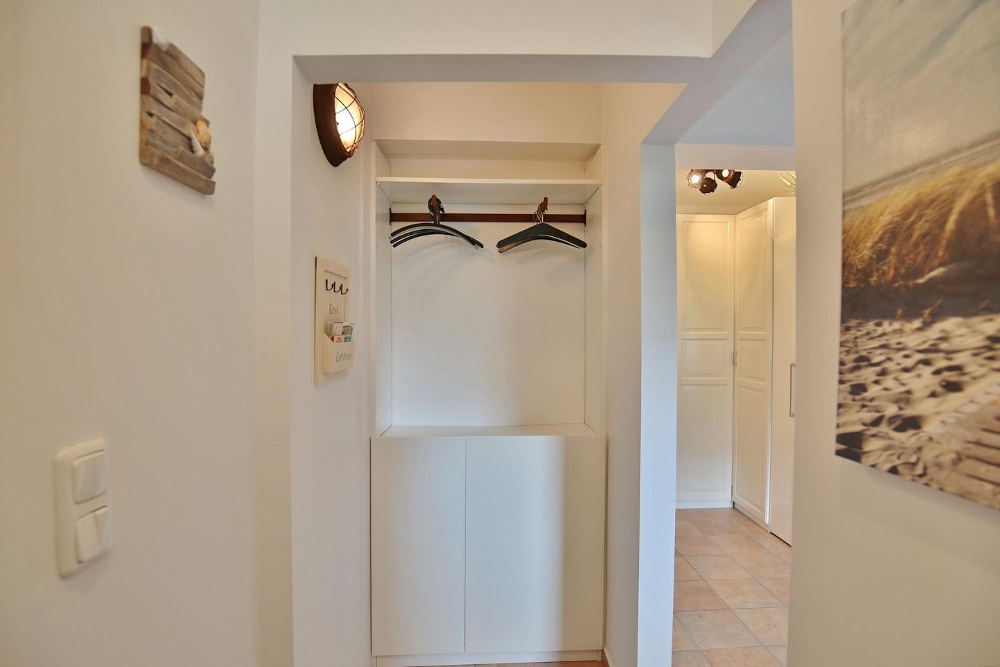 A hallway with a coat rack, a wall-mounted light fixture, and a door leading to another room.