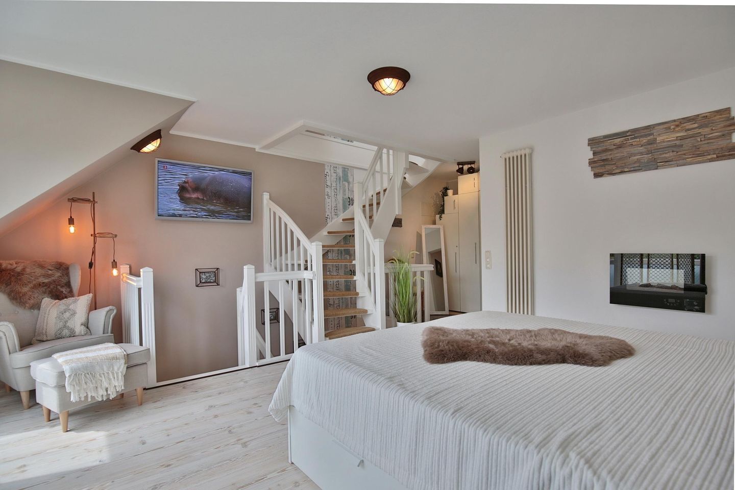 A bedroom with a large bed, a white staircase, a TV, and a cozy seating area with a fireplace.