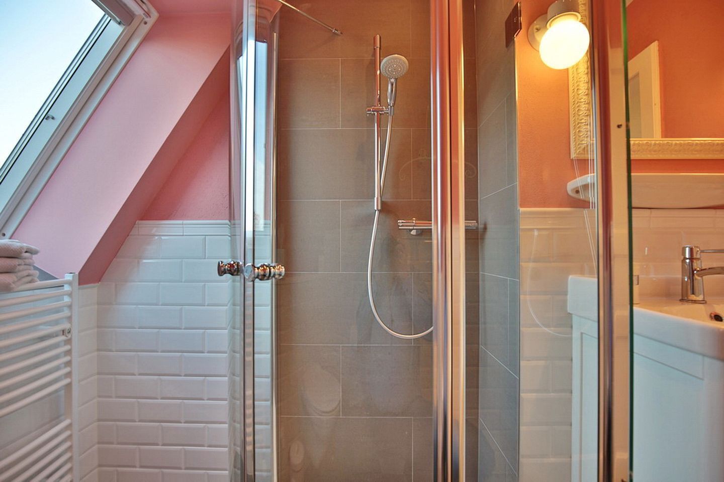 Una ducha moderna con puerta de vidrio, pared de azulejos blancos y un perchero visible.