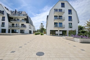 A modern apartment complex with multiple balconies, a paved courtyard, and a clear sky.