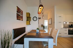 Un comedor moderno con una mesa de madera, sillas blancas y un banco negro. Hay estanterías de pared y un colgante de luz.