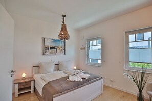 Un dormitorio con cama, mesitas de noche, lámpara colgante, ventana y un cuadro en la pared.