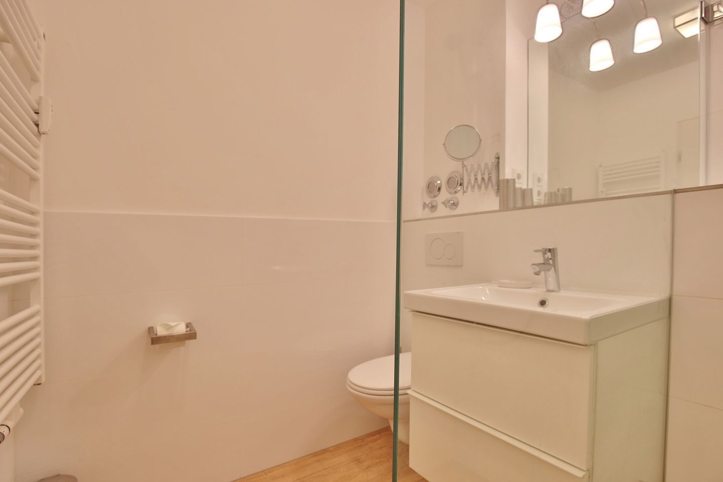 Un baño con mampara de vidrio, lavamanos blanco, espejo y un inodoro.