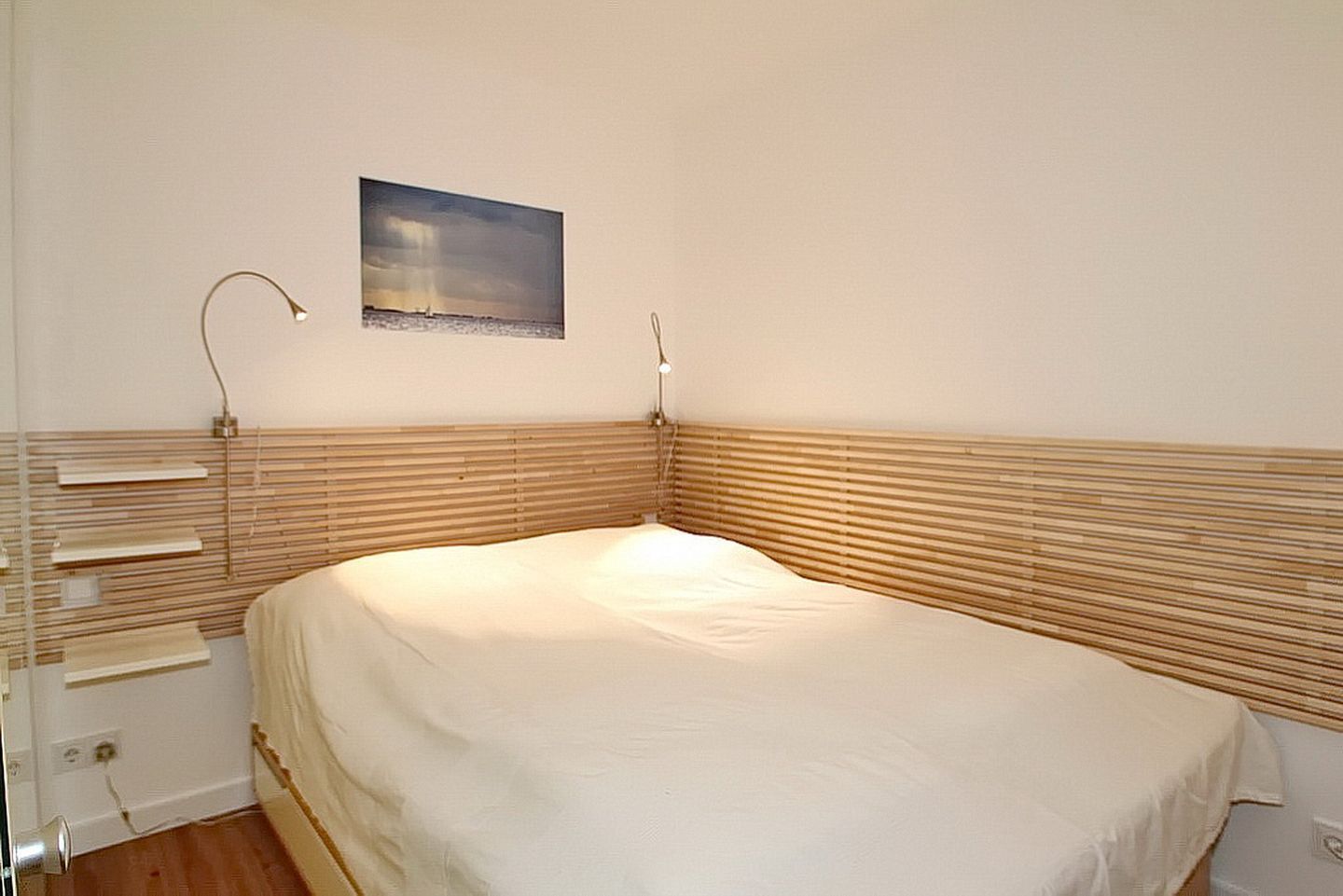 Ein Schlafzimmer mit Bett, Nachttischlampen, einem Nachttisch und einem Wandbild.