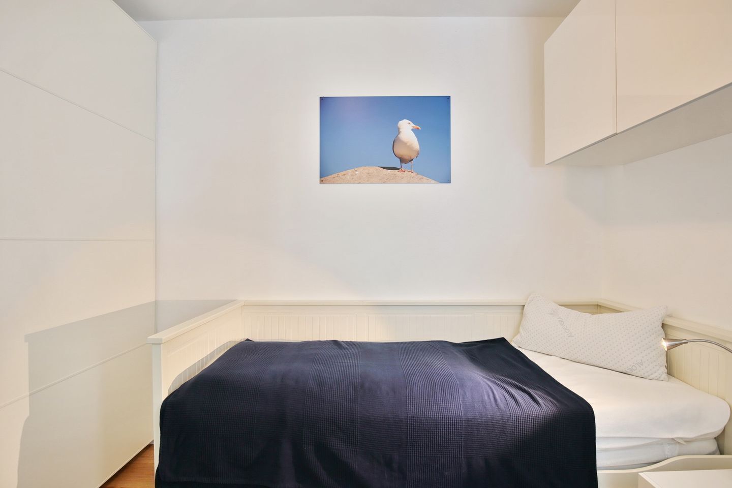 Un dormitorio con una cama, un almohadón y un cuadro enmarcado de una gaviota en la pared.