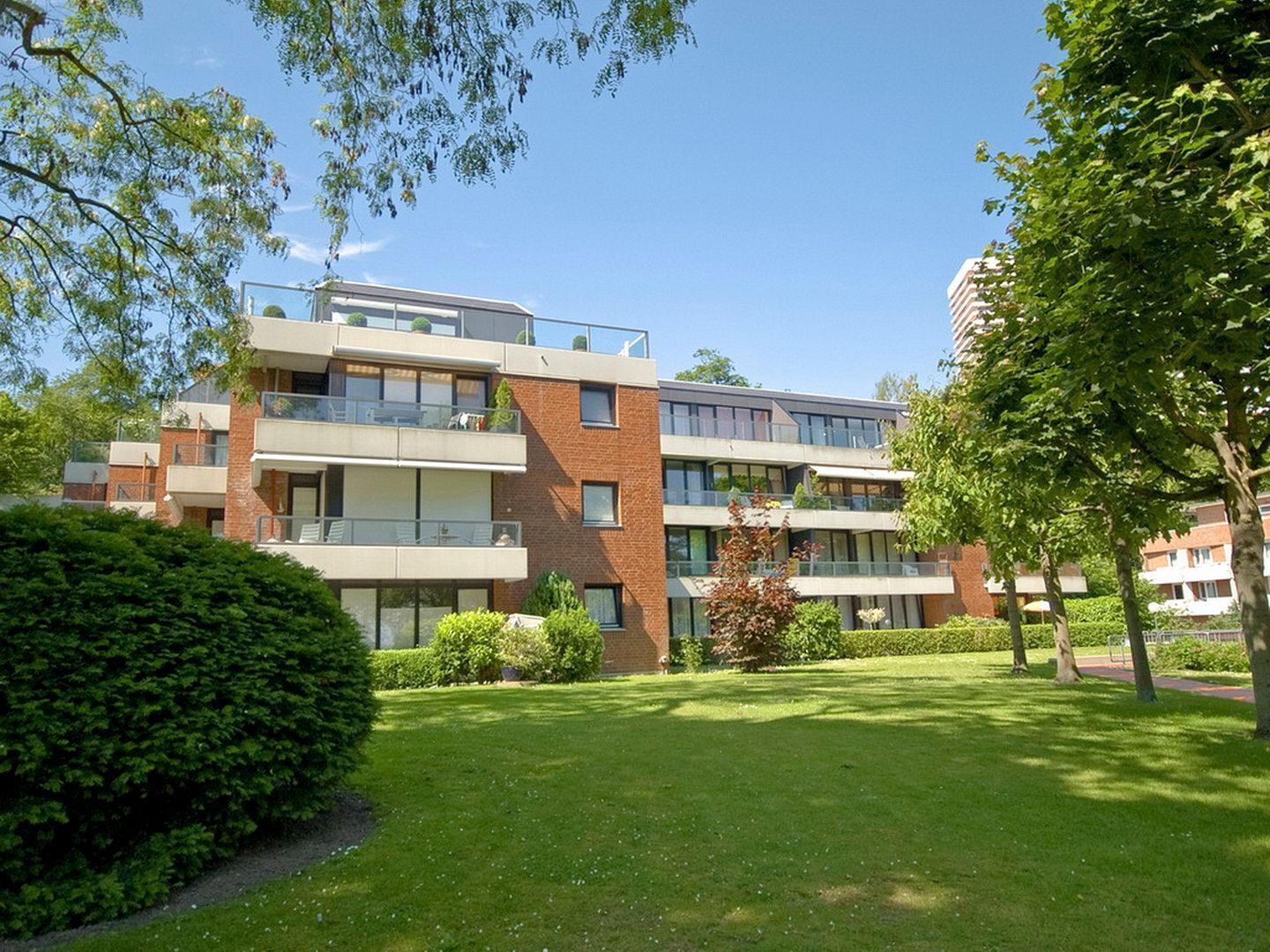 Een meerlaags woongebouw met balkons, een verzorgd gazon en omliggende bomen.