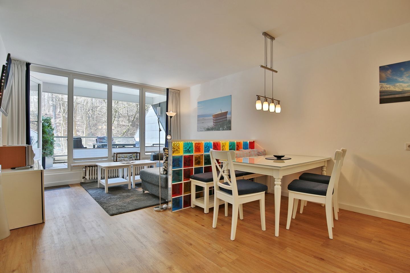 A modern kitchen with white cabinets, a dining table with four chairs, and a large window with a view of trees.