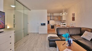 A modern apartment with a living room, kitchen, and a glass door leading to a balcony.