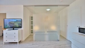 A modern room with a flat-screen TV on a white dresser, a sliding glass door closet, and a microwave on a white cabinet.